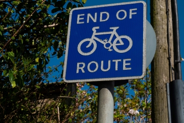 A sign saying 'end of cycle route', with trees behind it